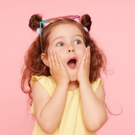 Portrait,Of,Surprised,Cute,Little,Toddler,Girl,In,Sunglasses,Over Portrait of surprised cute little toddler girl in sunglasses over pink background. Child model have fun and jump. Advertising childrens products